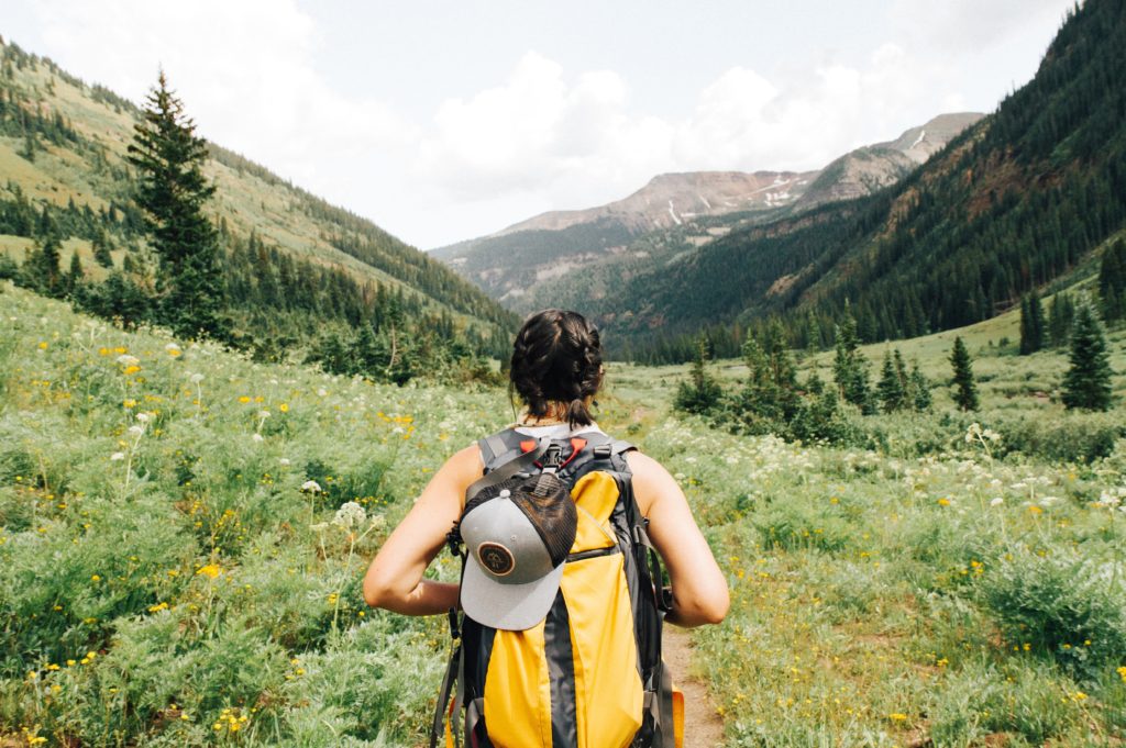 Women wearing backpack hiking in mountain scenery.