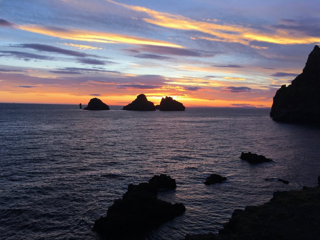 Sunset on ocean horizon with large rocks sticking out of water