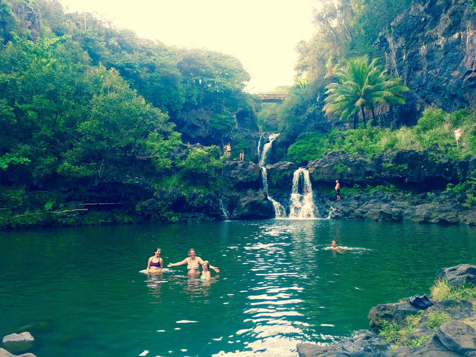 People swimming in natural pool of water with waterfall behind them