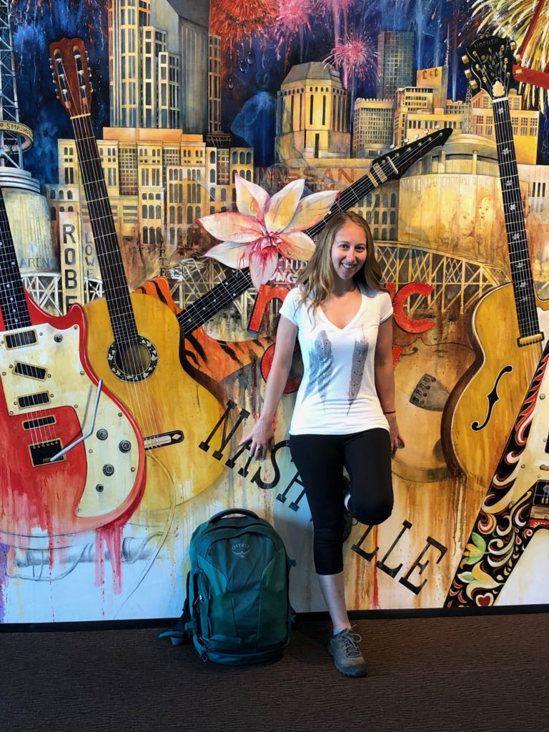 Alyssa leaning against Nashville mural. Osprey backpack is on floor next to Alyssa