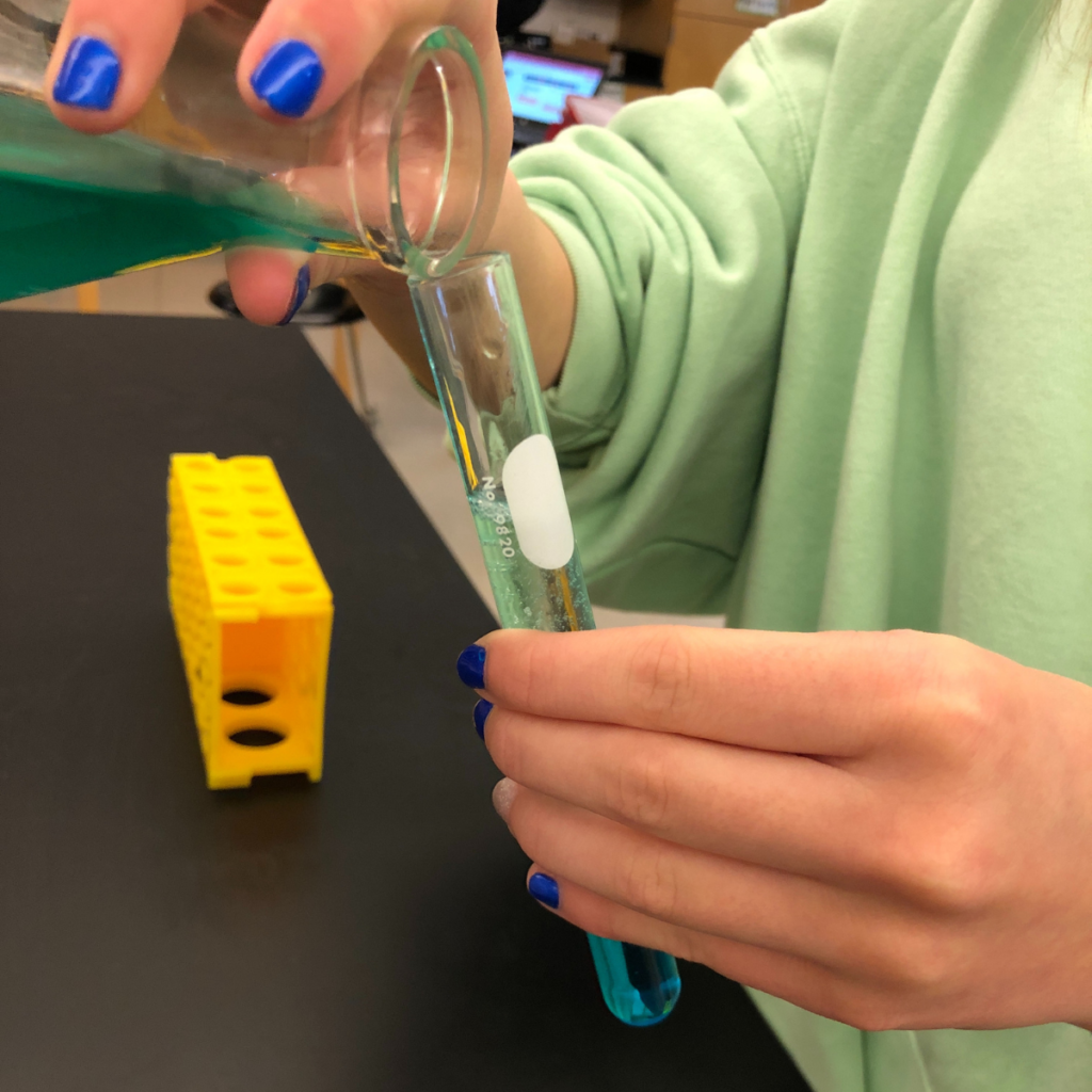 Student pours liquid from flask into a graduated cylinder.